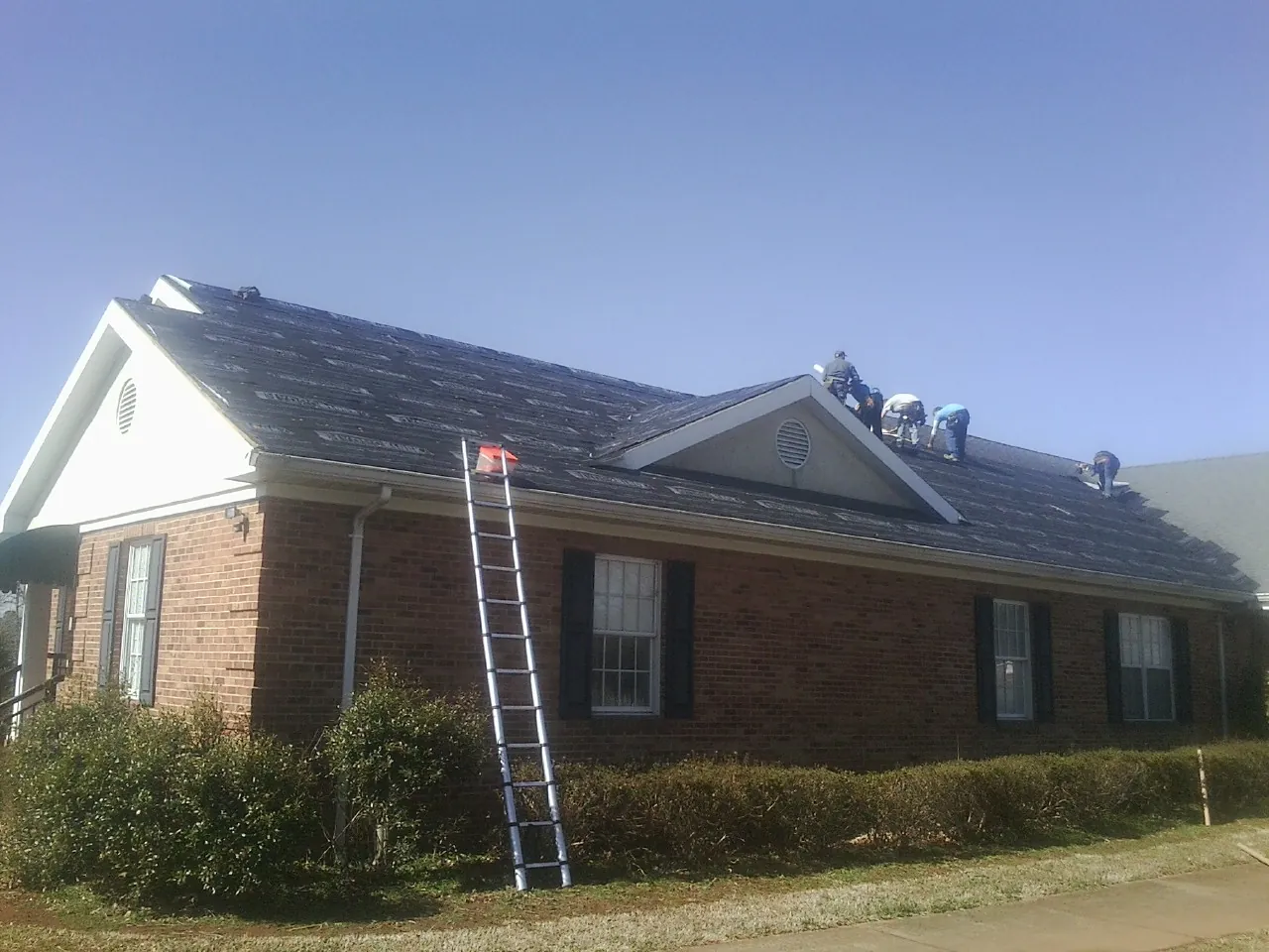 Crew tearing shingles off a brick ranch roof with a ladder set — Emergency Roof Repair work by our crew in Ladera Ranch