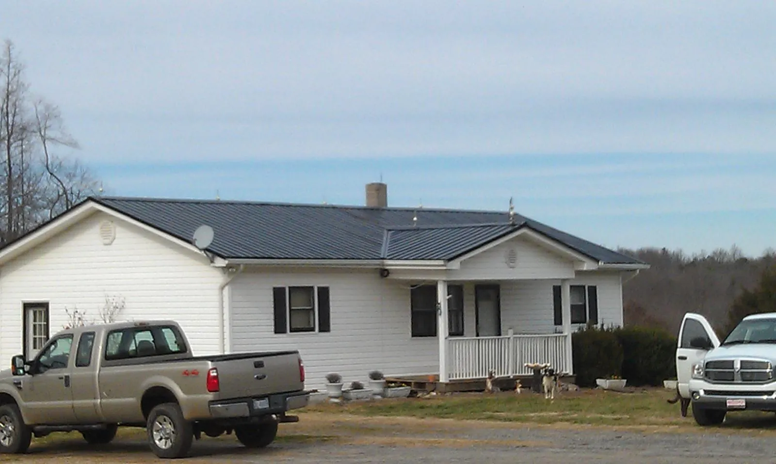 Finished dark metal roof on a white ranch home with work trucks parked in Ladera Ranch