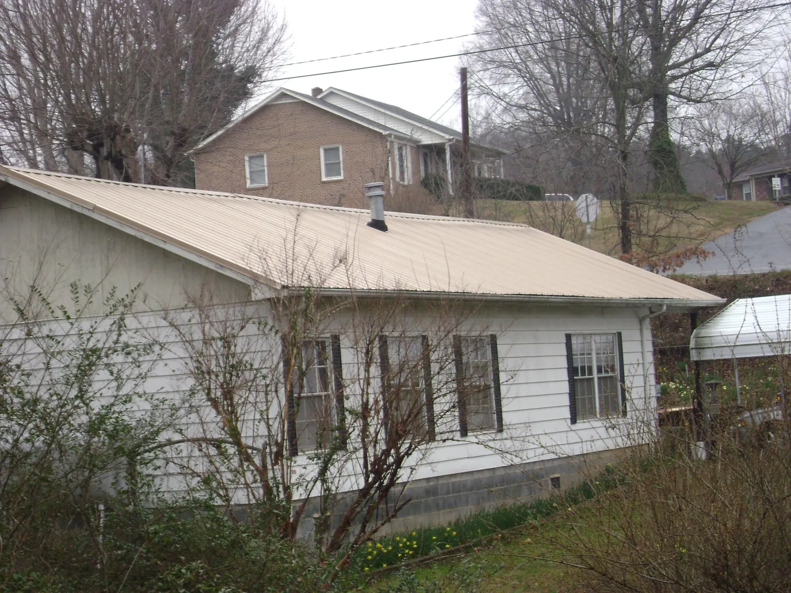 Tan metal roof on a white sided house set into a hillside — Commercial Roofing by Roofing Brothers in Ladera Ranch